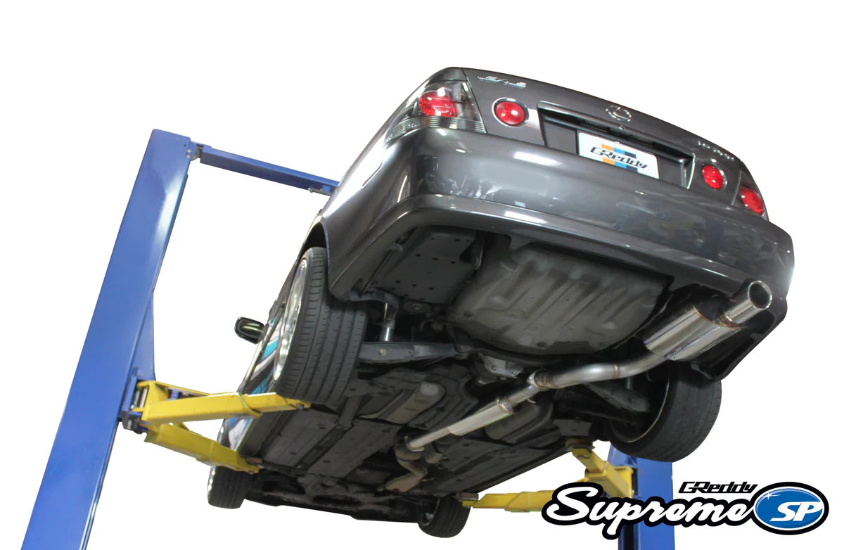 Underside view of a Lexus IS300 featuring the full GReddy Supreme SP catback exhaust system, showing the seamless routing from the catalytic converter to the rear bumper